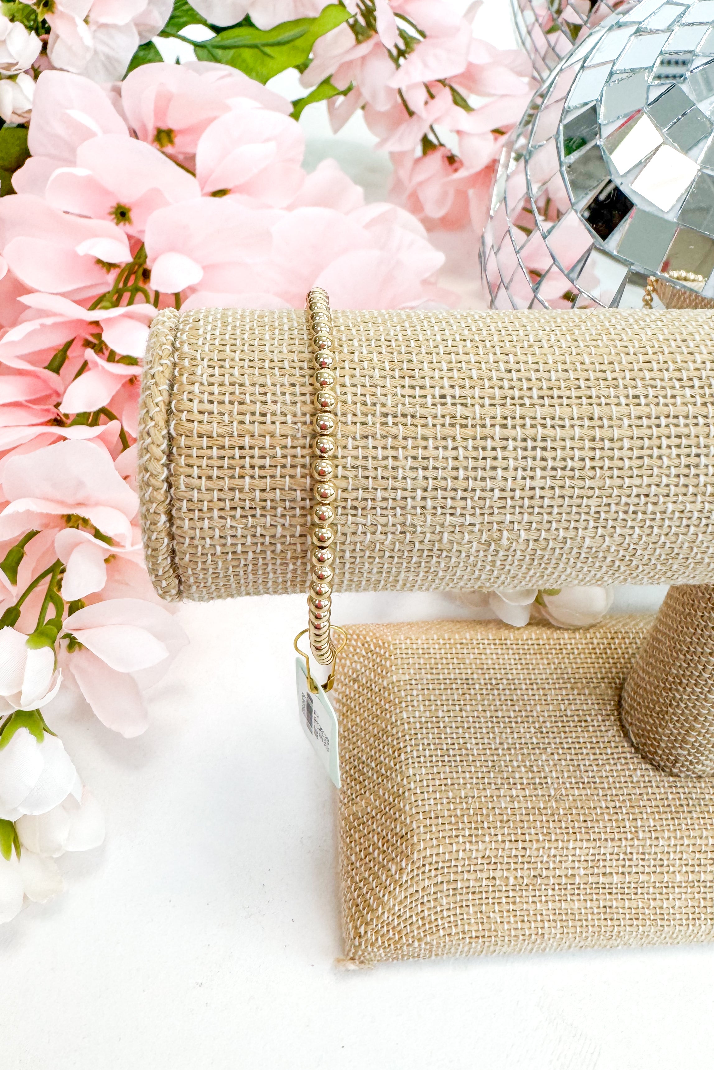 gold enewton bracelet on burlap display with floral background