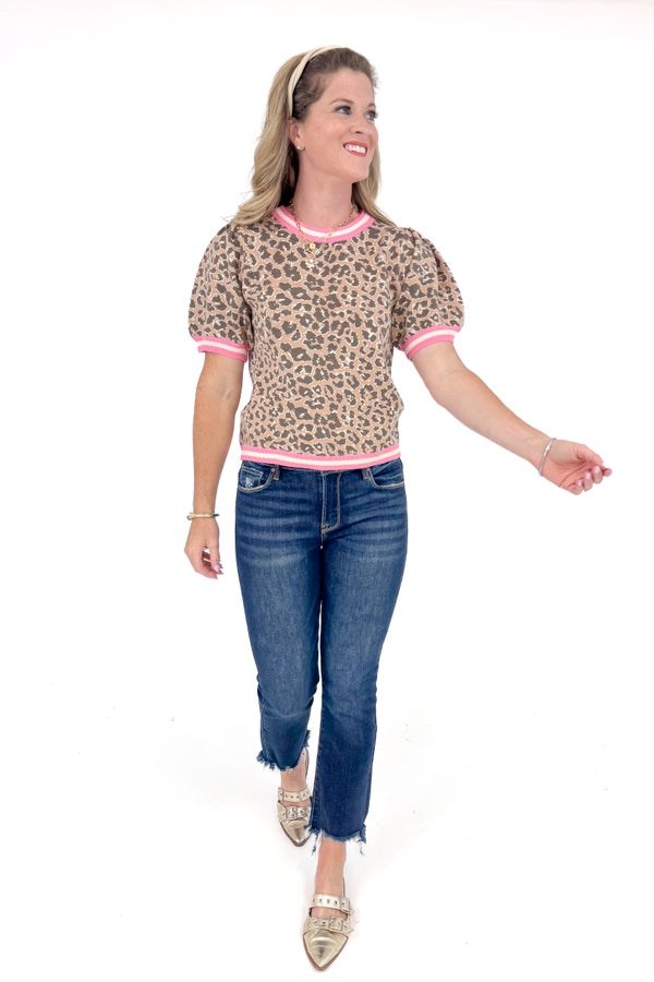 Woman wearing a leopard print top with pink trim and blue jeans on a white background