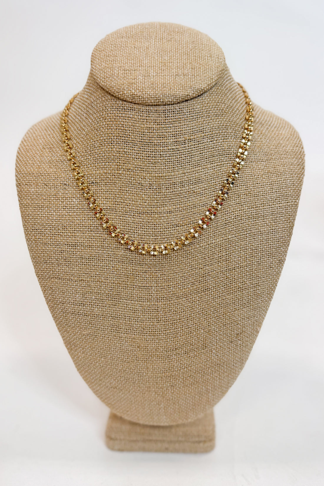 Gold necklace on a beige bust against a white background