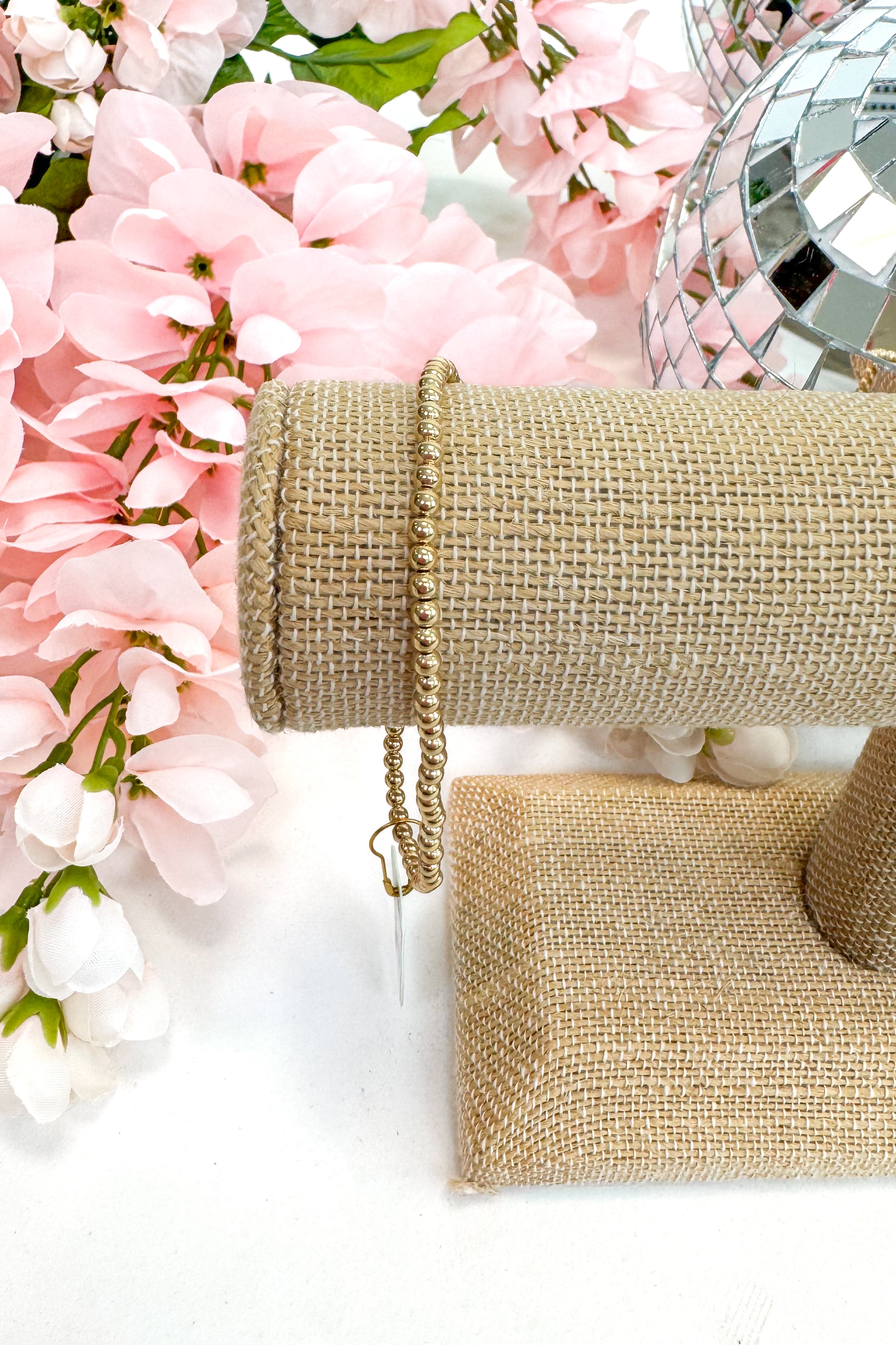 gold enewton bracelet on burlap display with floral background