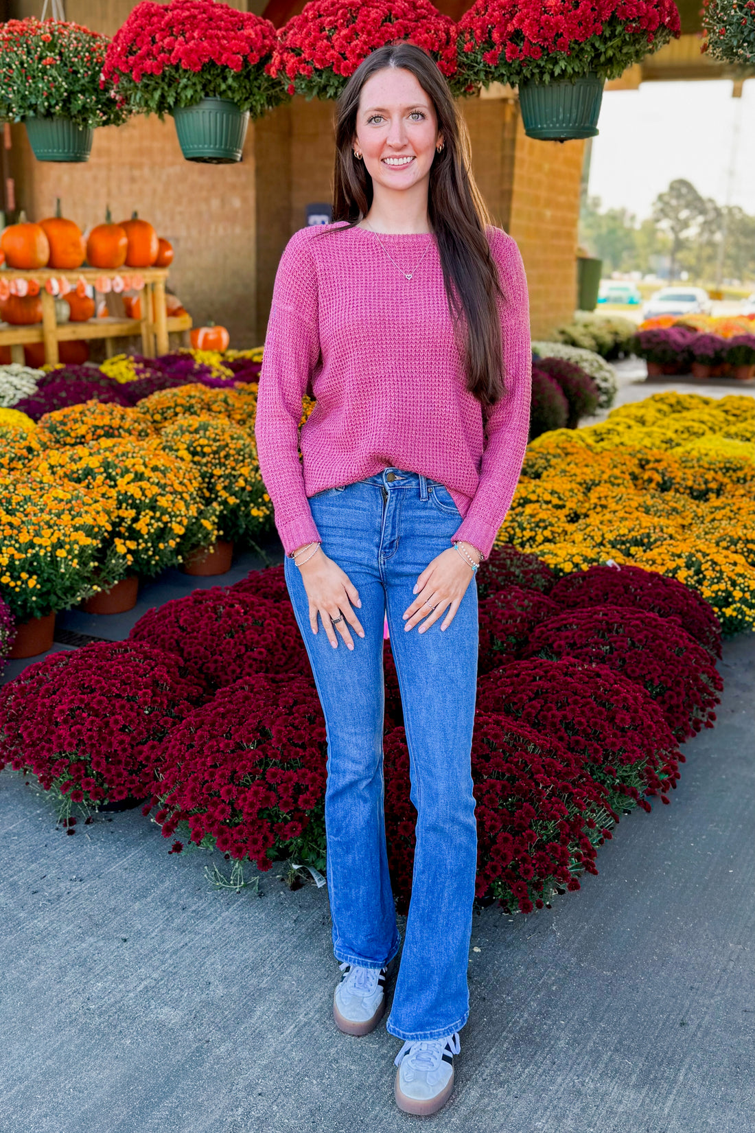 Outdoor picture of woman wearing Rose Waffle Knit Sweater and jeans with mums in the background. 