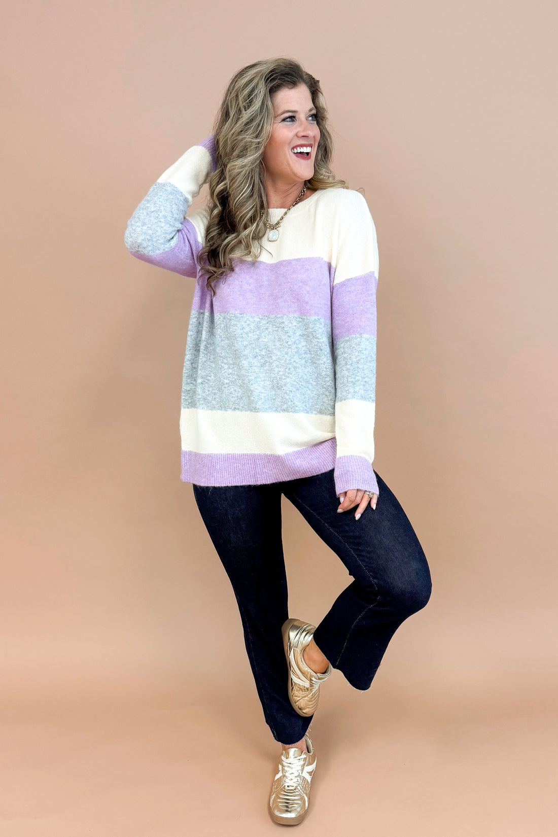 Woman wearing Lavender & Grey Colorblock Sweater and jeans with tan background.