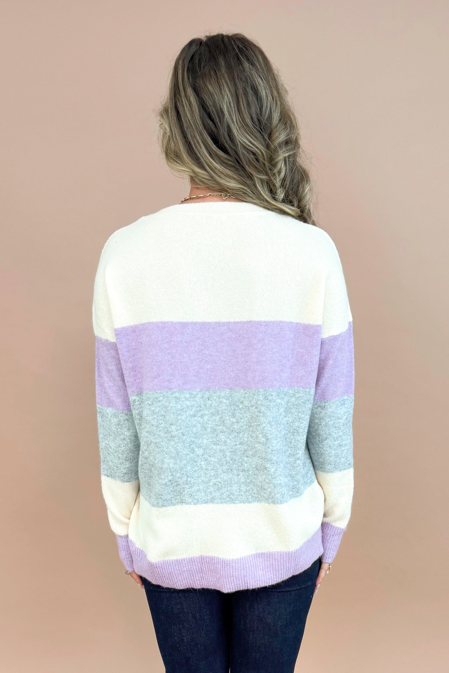 Back view of woman wearing Lavender &amp; Grey Colorblock Sweater and jeans with tan background.