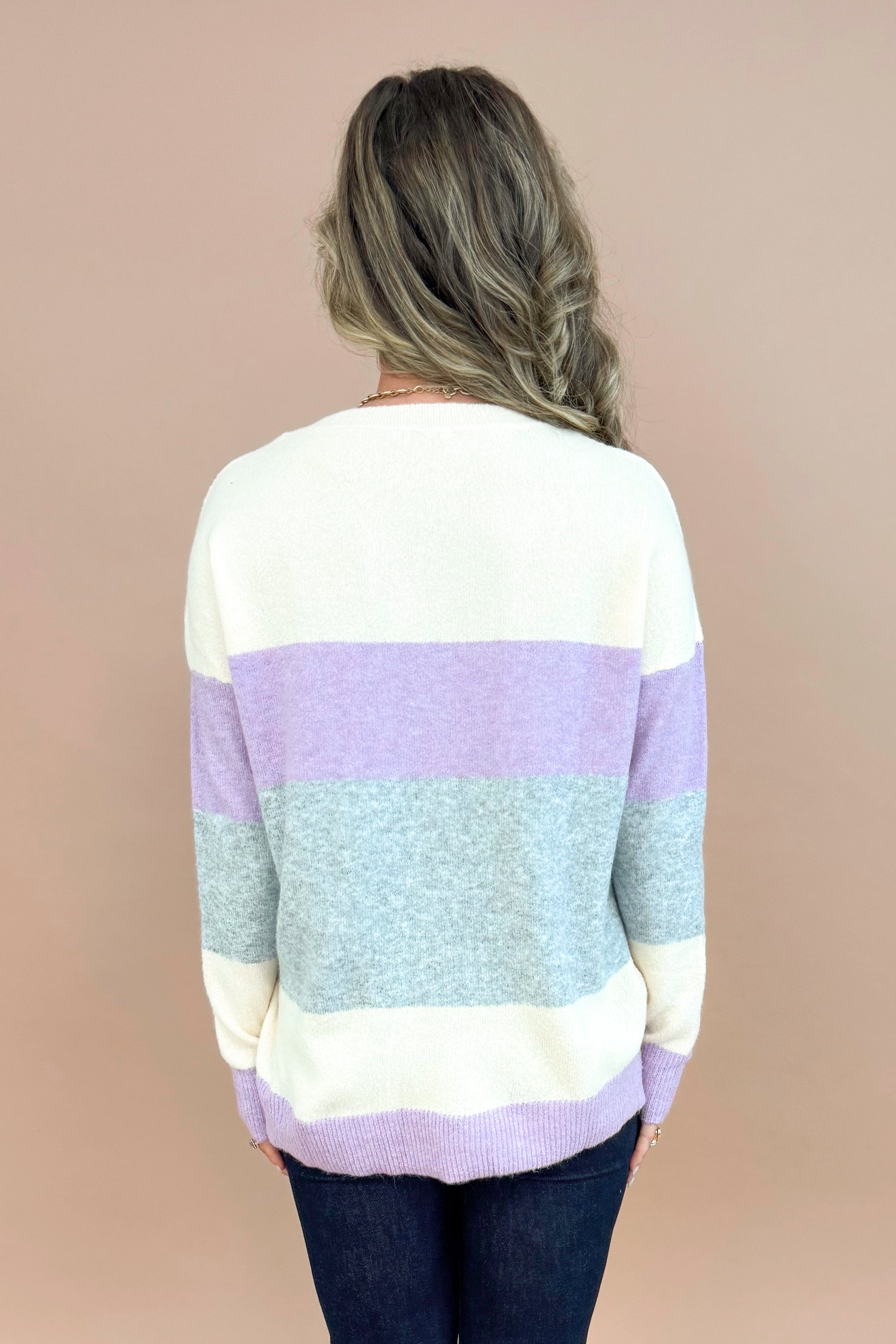 Back view of woman wearing Lavender &amp; Grey Colorblock Sweater and jeans with tan background.
