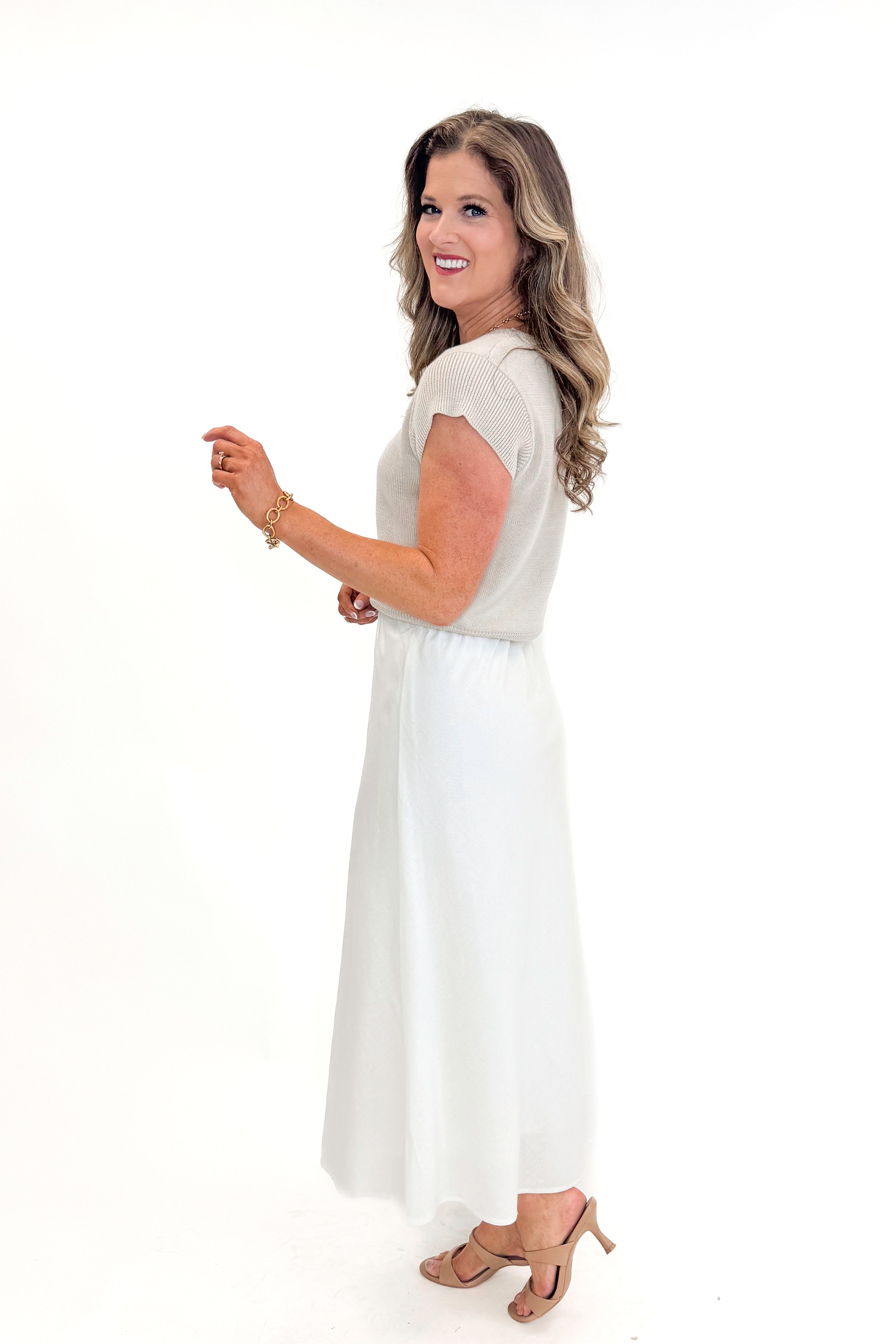 Side view of woman wearing Beige Cap Sleeve Sweater with skirt against white studio background.