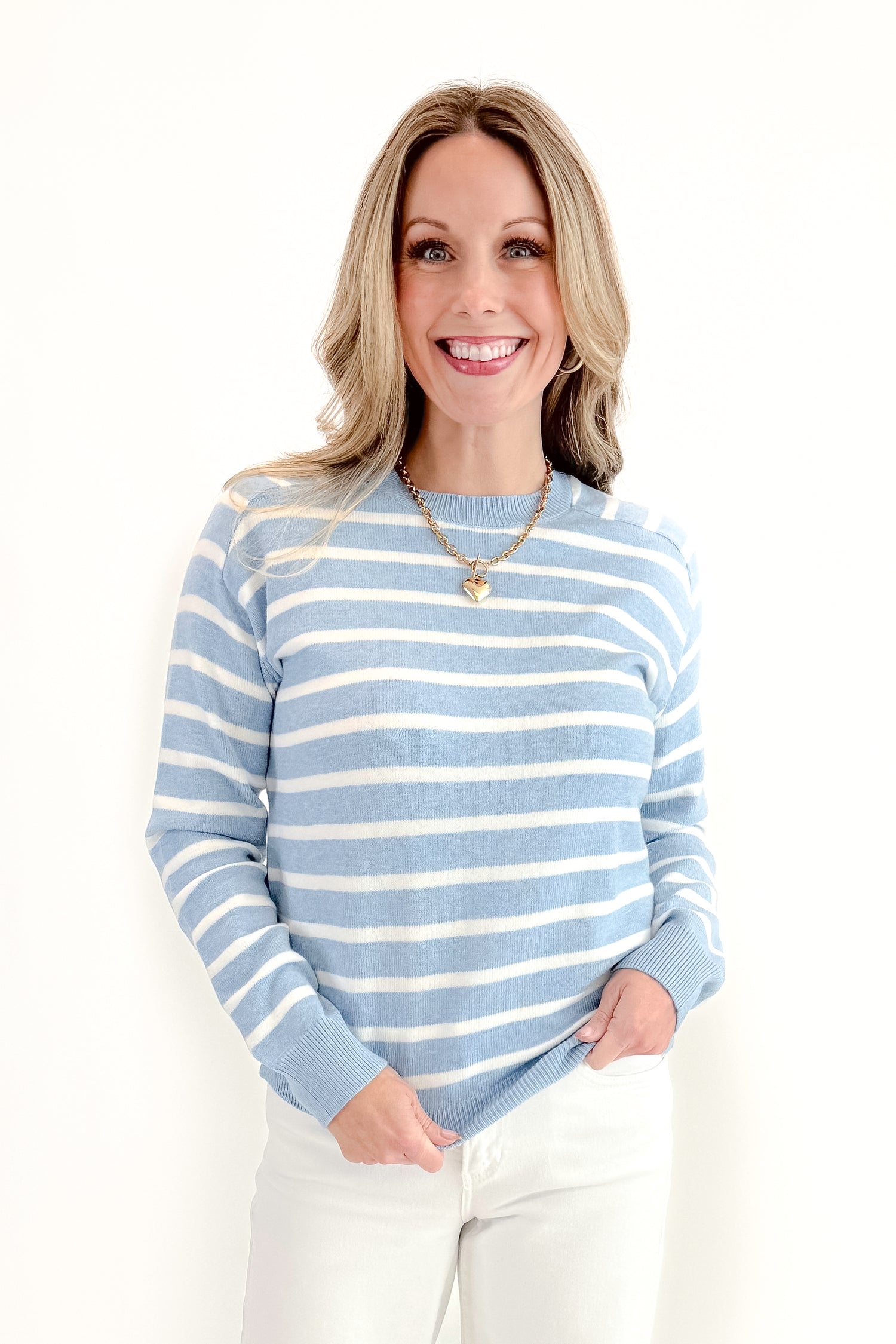 Front view of woman wearing Light Blue Striped Sweater with jeans against a white background.