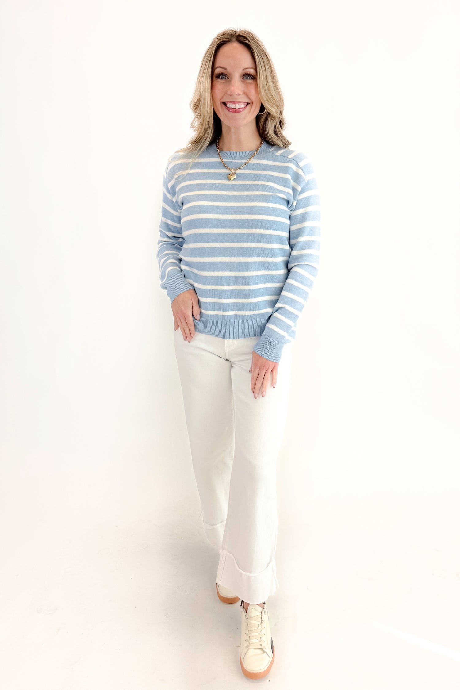 Front view of woman wearing Light Blue Striped Sweater with jeans against a white background.