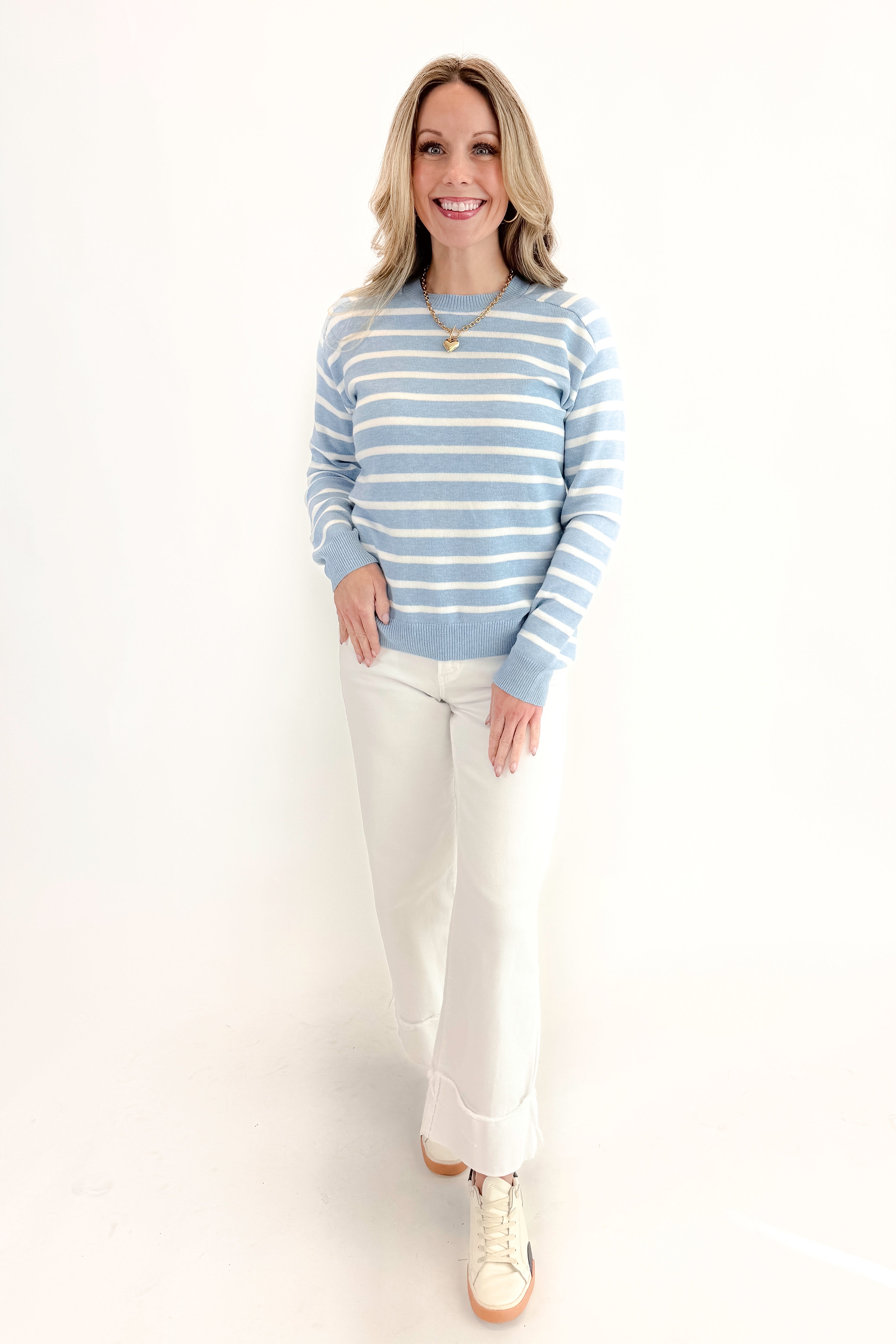 Front view of woman wearing Light Blue Striped Sweater with jeans against a white background.