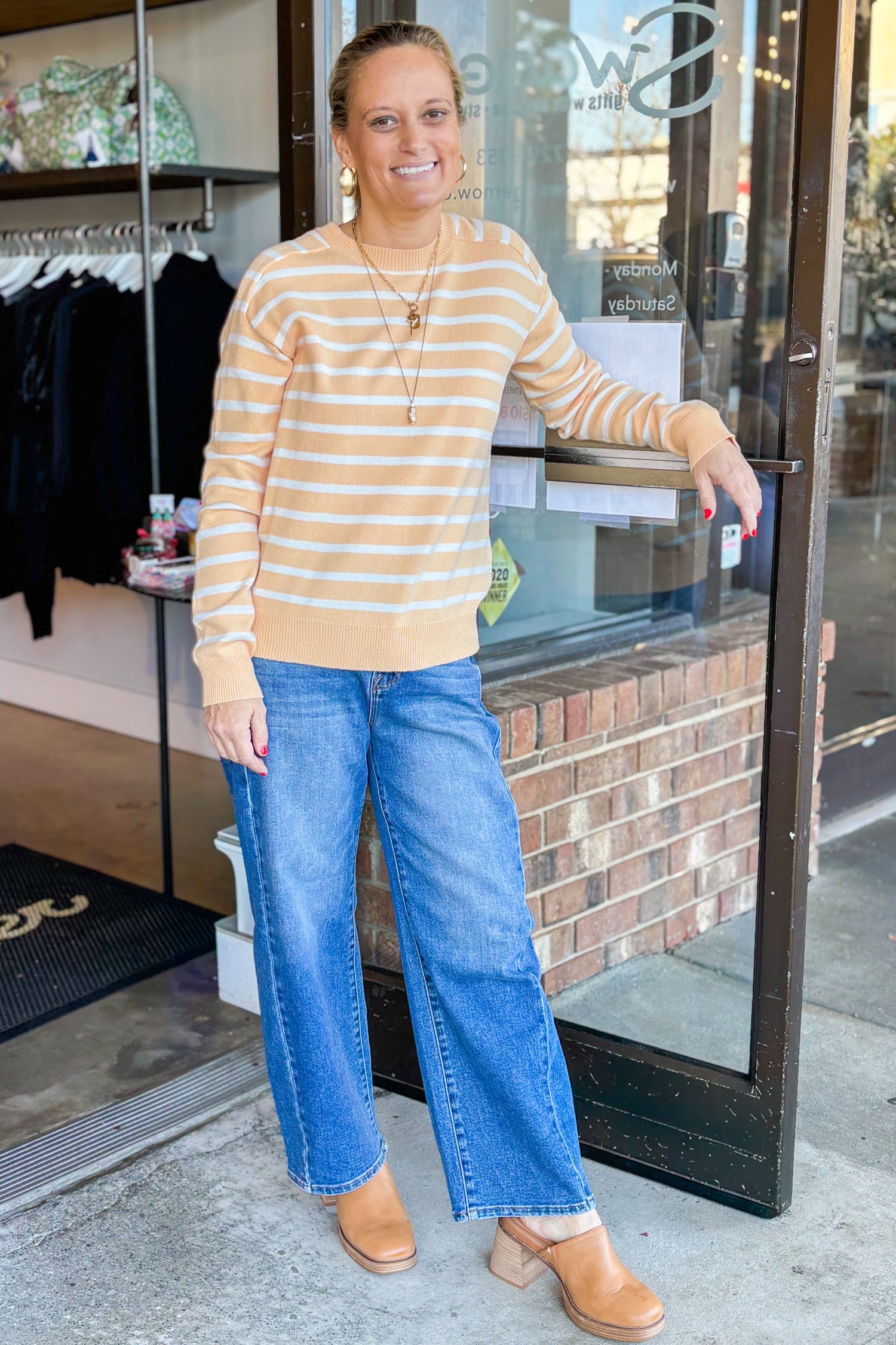 Front view of woman wearing Yellow Striped Sweater with jeans at a boutique by the front door.