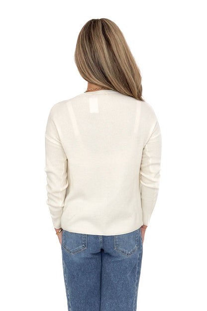Back view of woman wearing Ivory Textured Pocket Detail Sweater with jeans against white studio background.
