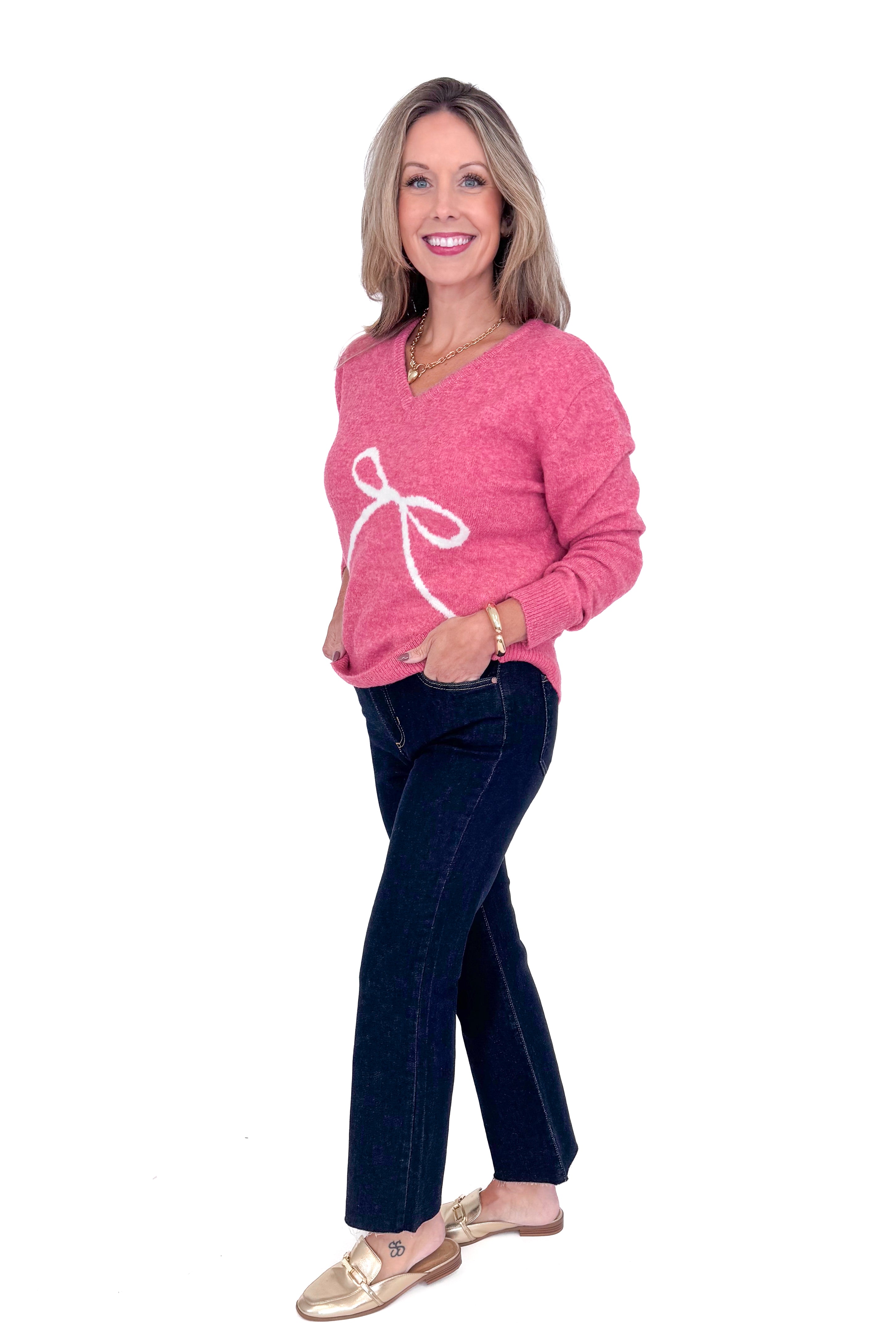 Side view of woman wearing Pink Bow Printed Sweater and blue jeans. 