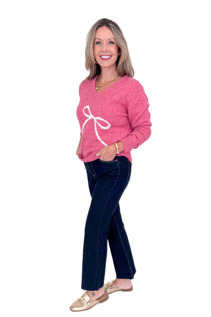 Side view of woman wearing Pink Bow Printed Sweater and blue jeans. 