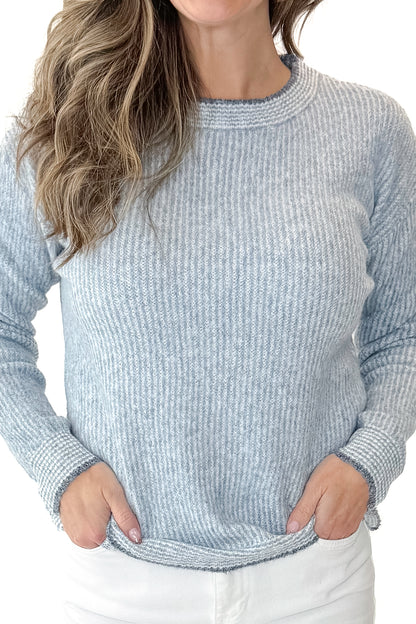 Detail view of woman wearing Light Blue Ribbed Sweater with white jeans against a white background.