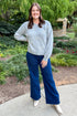 Front view of woman outside with greenery around wearing Grey Pearl Bow Detail Sweater and jeans.  