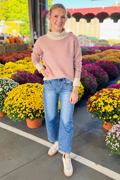 Outside picture of woman wearing Mauve Striped Turtleneck Sweater and blue jeans with mums in the background.