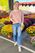 Outside picture of woman wearing Mauve Striped Turtleneck Sweater and blue jeans with mums in the background.