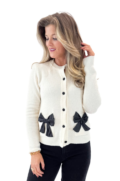 Front view of woman wearing Ivory Bow Pocket Detail Cardigan with jeans against white studio background.