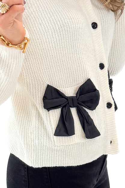 Front detail view of woman wearing Ivory Bow Pocket Detail Cardigan with jeans against white studio background.