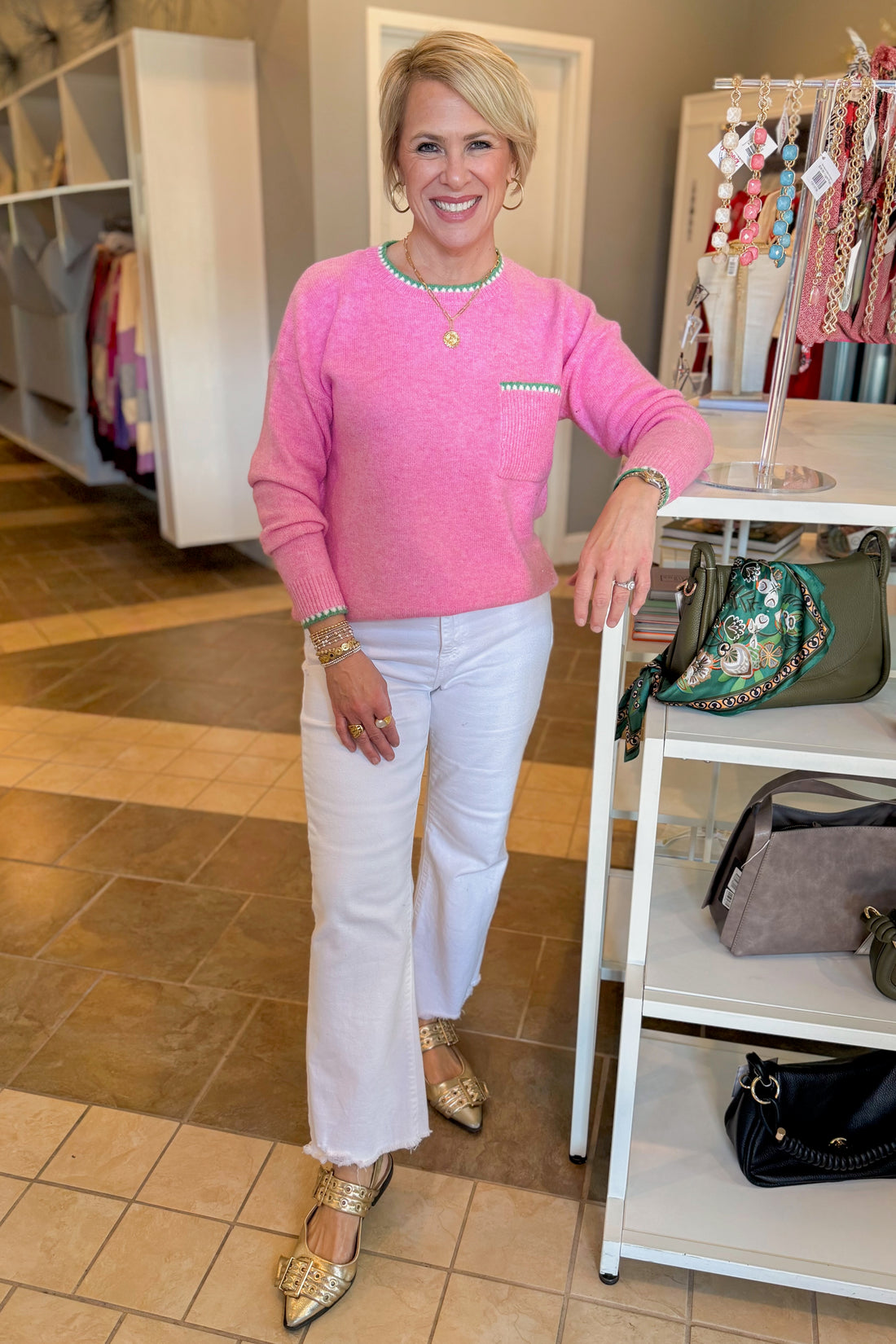 Front view of woman wearing Pink With Green Stitching Sweater with jeans at a boutique.