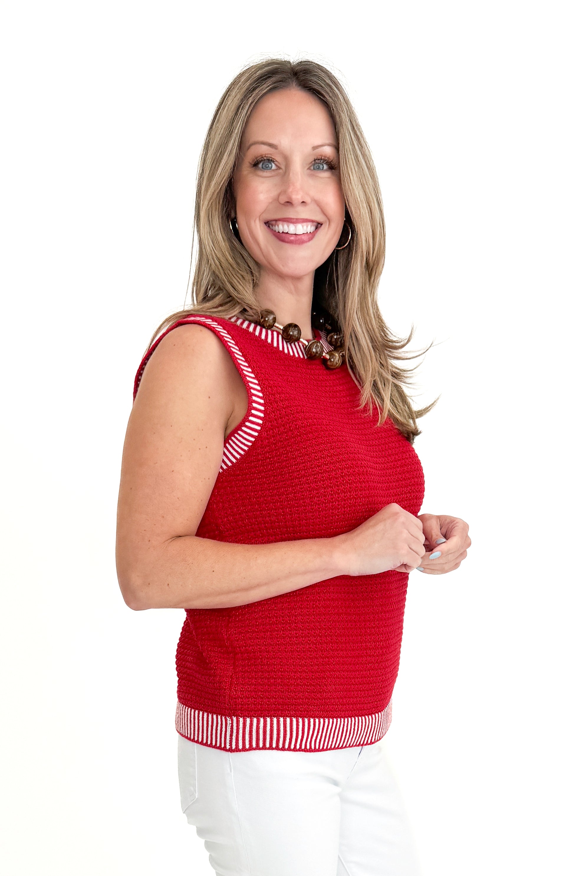Side view of woman wearing Red &amp; White Textured Sweater Tank with jeans against white studio background.