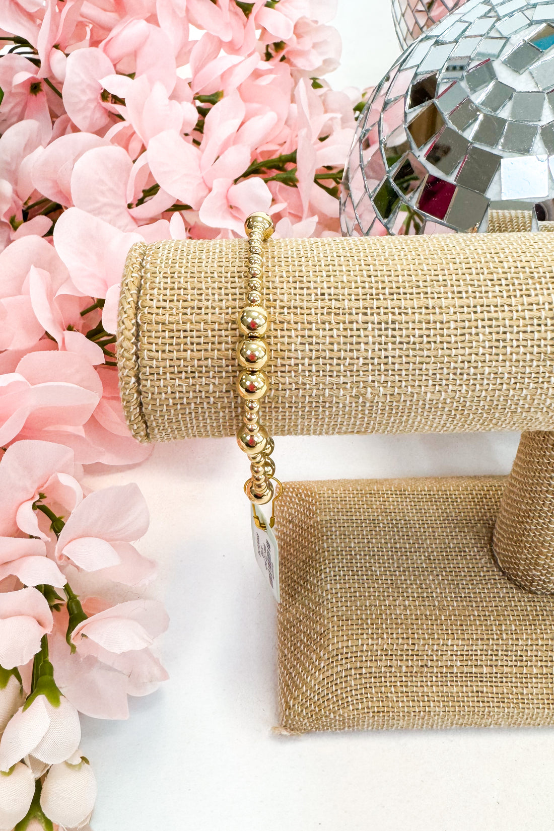 Gold bracelet on a jewelry stand with pink flowers and a disco ball in the background