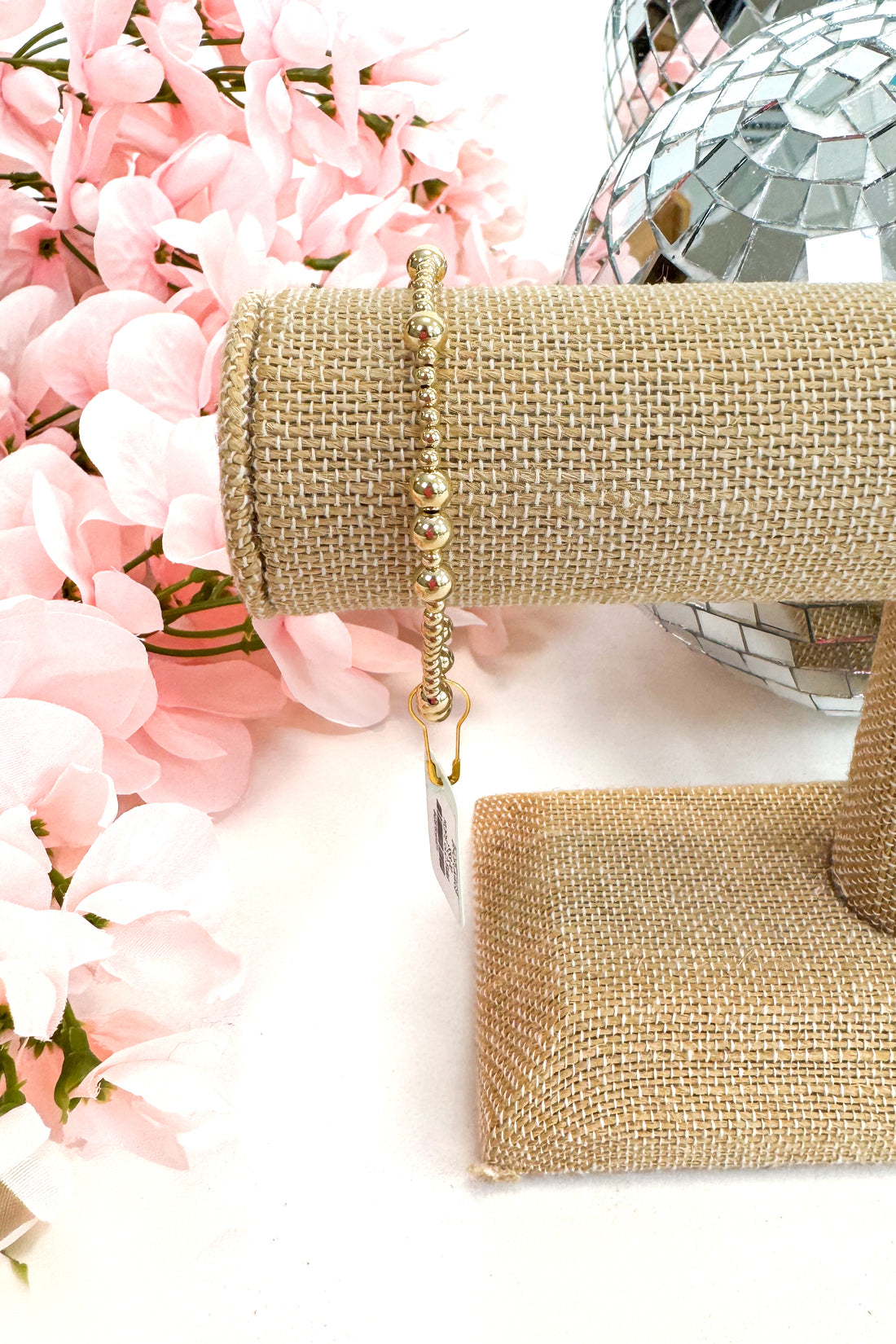 Gold bracelet on a burlap-wrapped wrist with pink flowers and a disco ball in the background