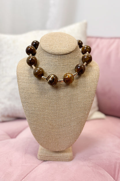 Necklace with brown beads on a beige bust against a pink background