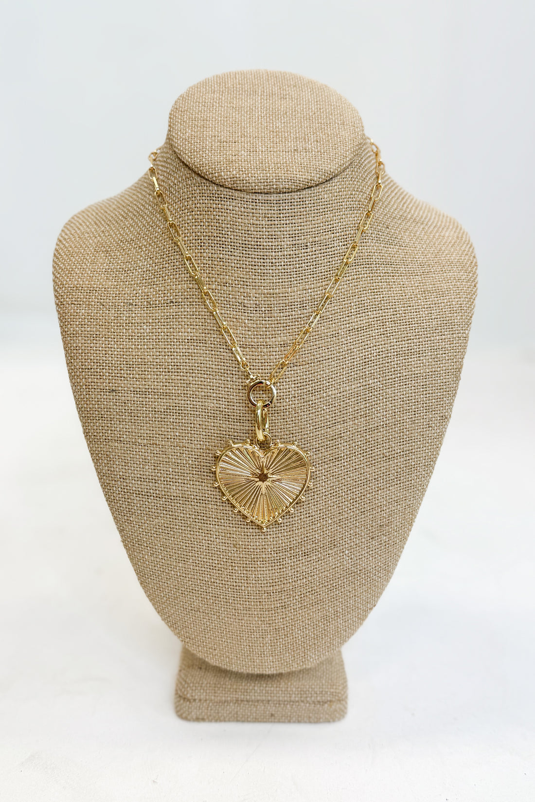 Gold necklace with a heart-shaped pendant on a beige mannequin bust against a white background