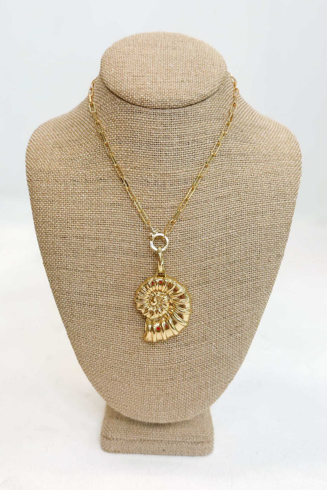 Gold necklace with a pendant on a beige mannequin bust against a white background
