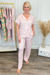 Woman wearing a pink floral pajama set standing in a room with a rack of pajamas and decorative elements.
