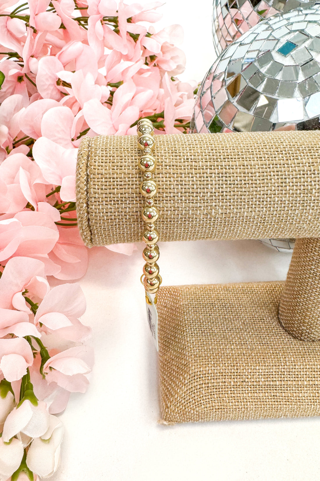 Gold bracelet on a jewelry stand with pink flowers in the background
