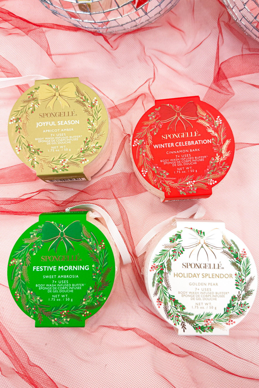 Four Spongelle holiday-themed product containers on a pink sheer fabric background