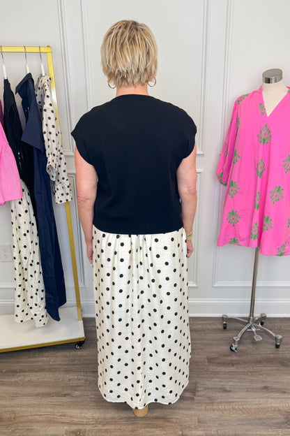 Back view of woman wearing Swagger Boutique’s Black &amp; Cream Polka Dot Layered Midi Dress by Entro with sandals at the store. 