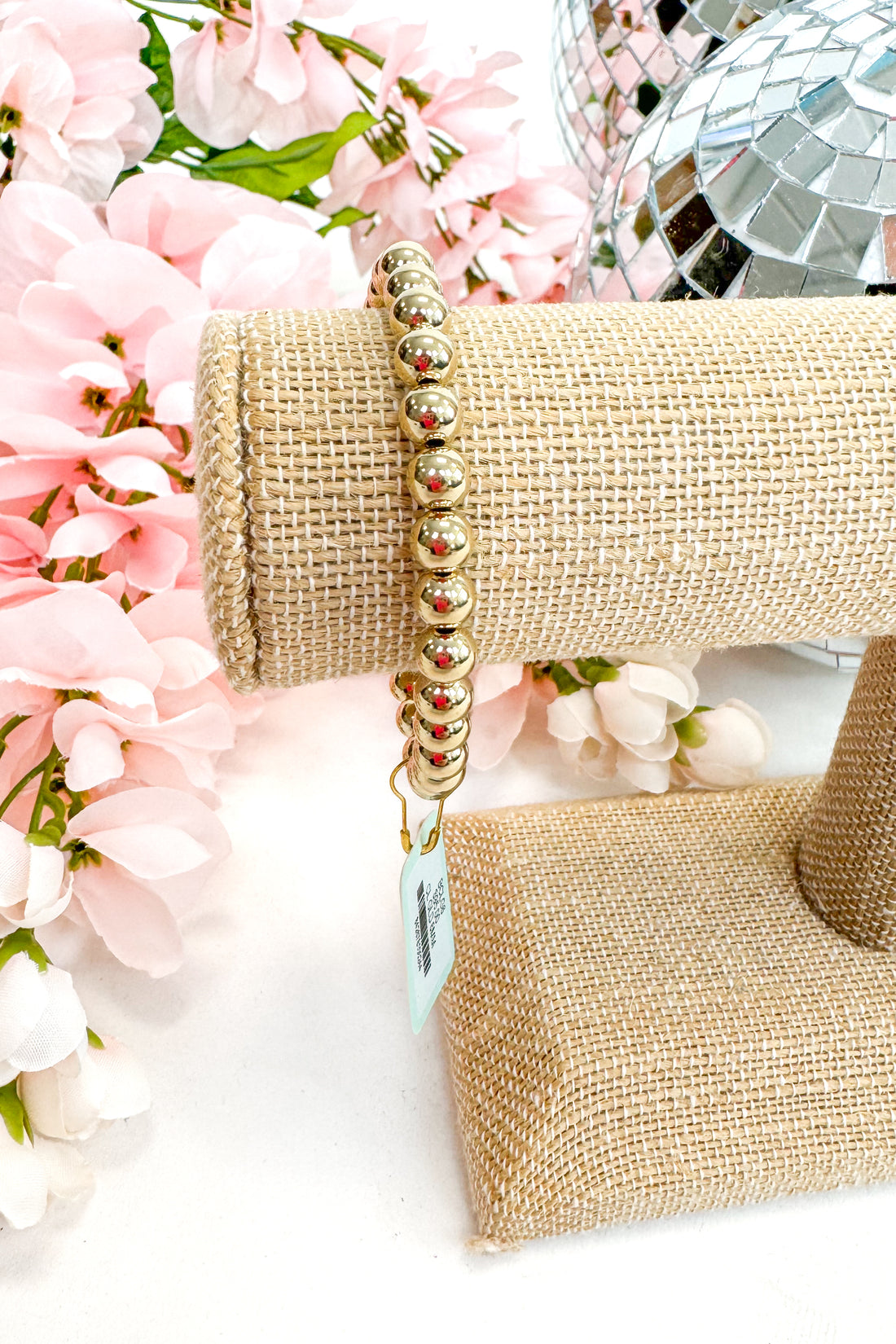 gold enewton bracelet on burlap display with floral background