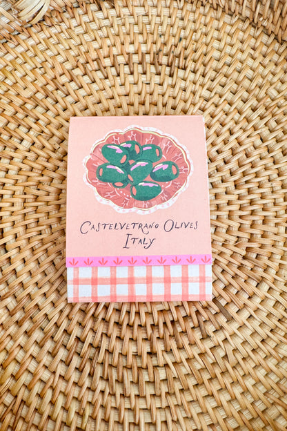 Small pink packaging with olive design on a woven surface
