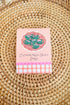 Small pink packaging with olive design on a woven surface