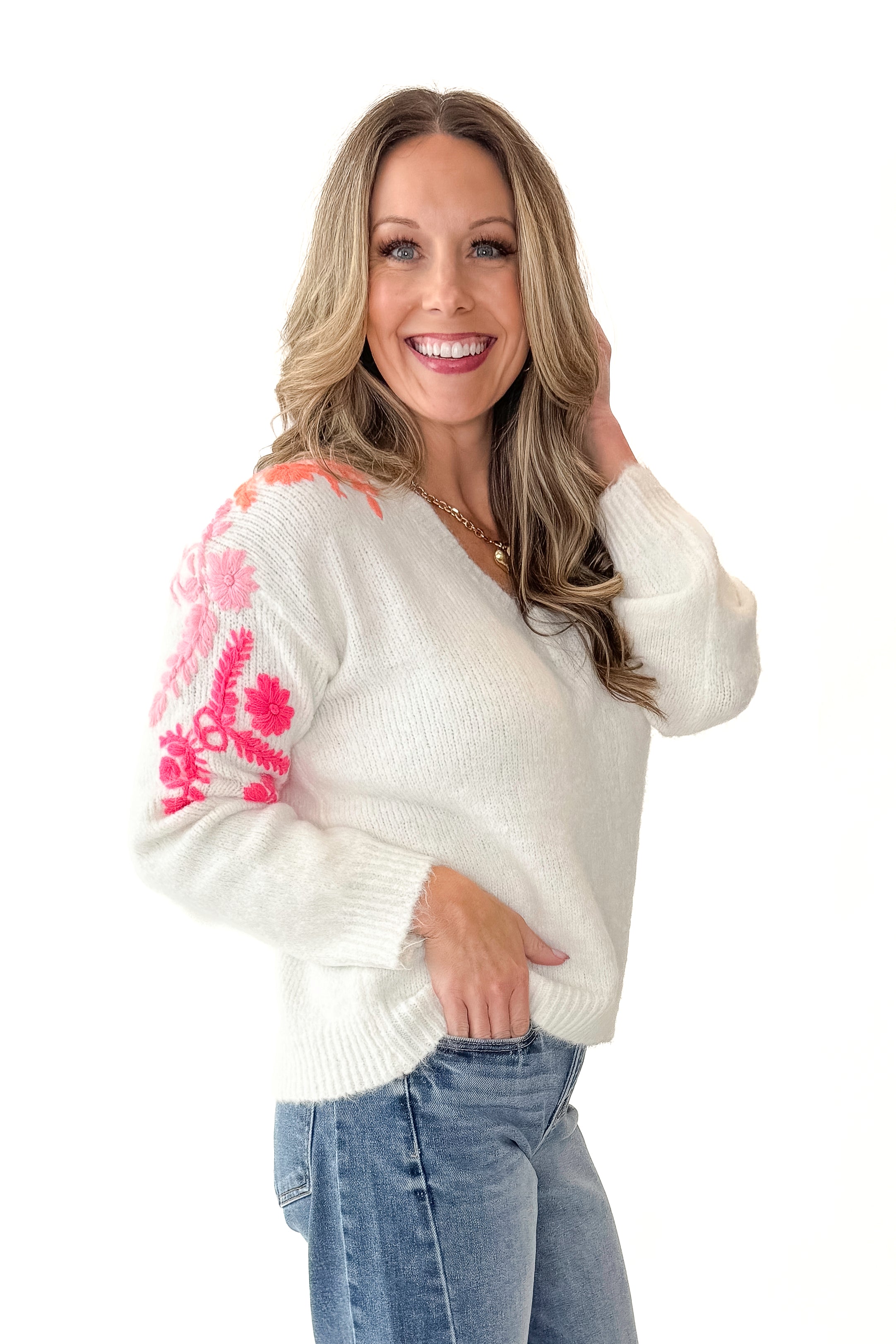 Side view of woman wearing Ivory With Floral Embroidery Sweater with jeans against white studio background.