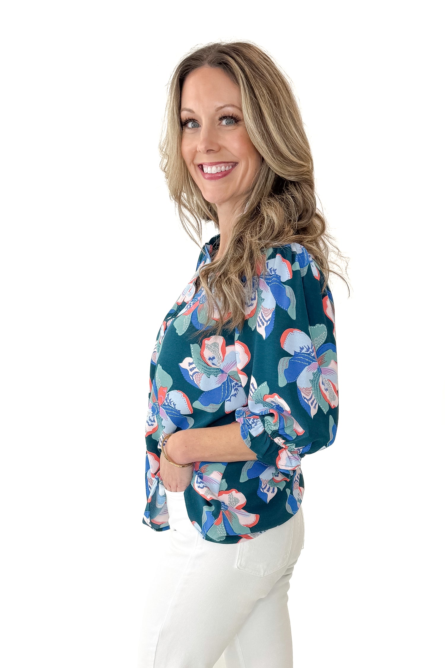 Side view of woman wearing Green &amp; Pink Floral Julie Top with jeans against white studio background.