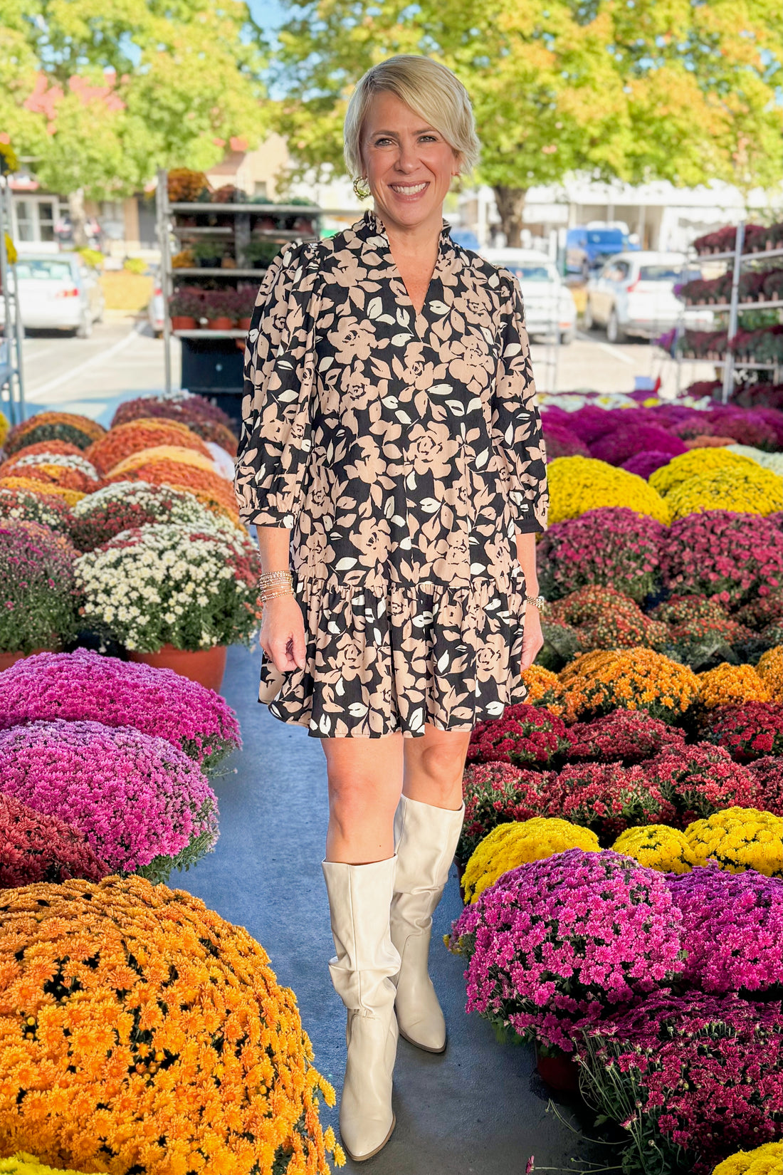 Outdoor picture of woman wearing Ready Set Grow Naomi Dress In Black &amp; Tan by Mary Square with mums in the background.