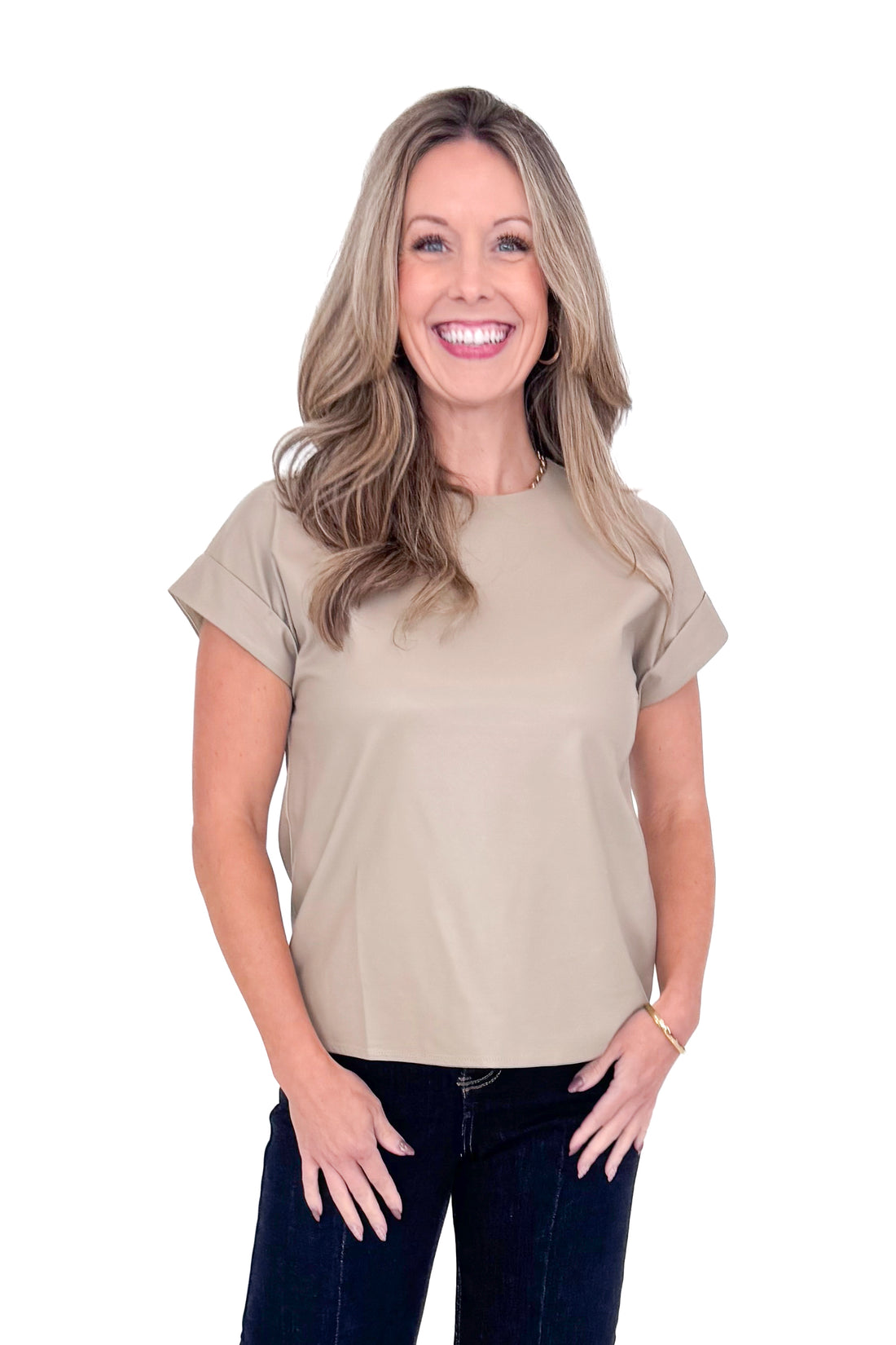 Front view of woman wearing taupe faux leather top with jeans against white studio background.