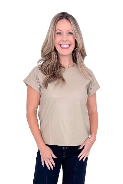 Front view of woman wearing taupe faux leather top with jeans against white studio background.