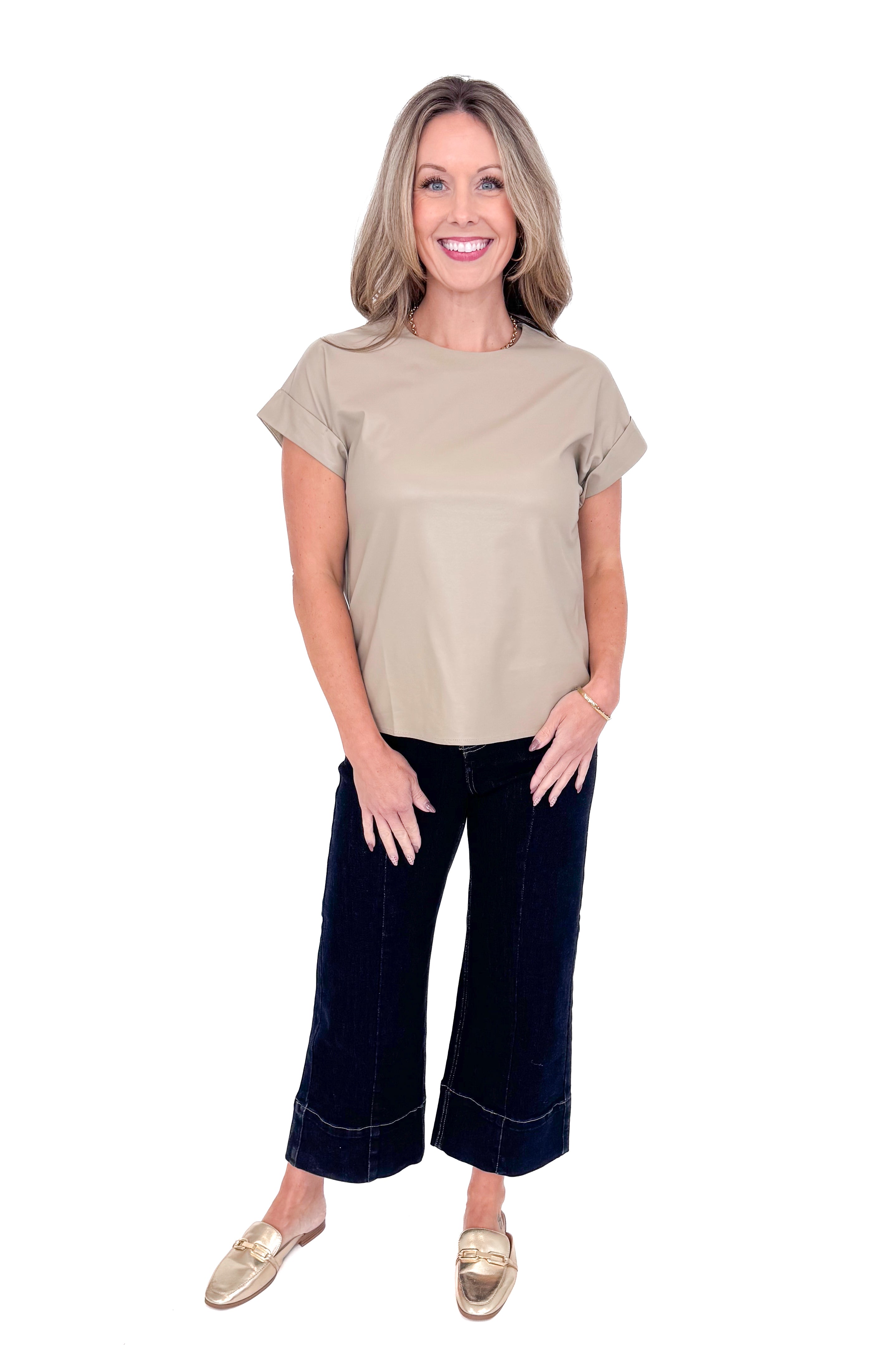 Front view of woman wearing taupe faux leather top with jeans against white studio background.