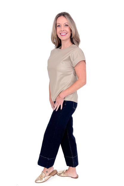 Side view of woman wearing taupe faux leather top with jeans against white studio background.