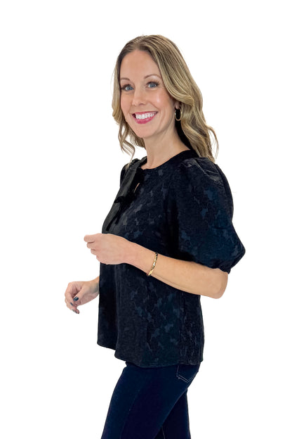 Side view of woman wearing Black Lace Ren Top with jeans against white studio background.