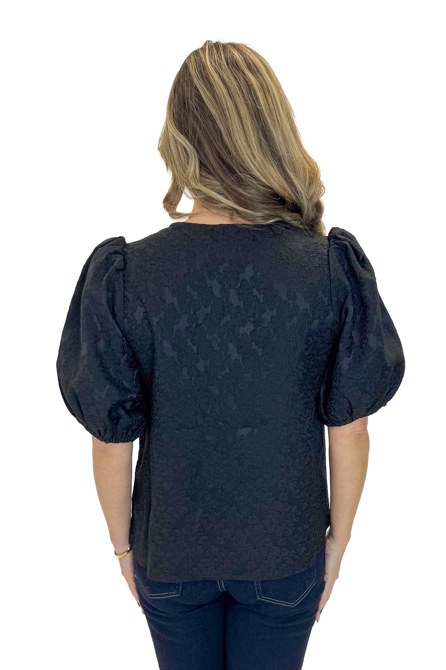 Back view of woman wearing Black Lace Ren Top with jeans against white studio background.