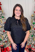 Front view of woman wearing Black Lace Ren Top with jeans against holiday decor.