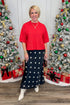 Woman in a red top and polka dot skirt standing in front of Christmas trees with decorations.