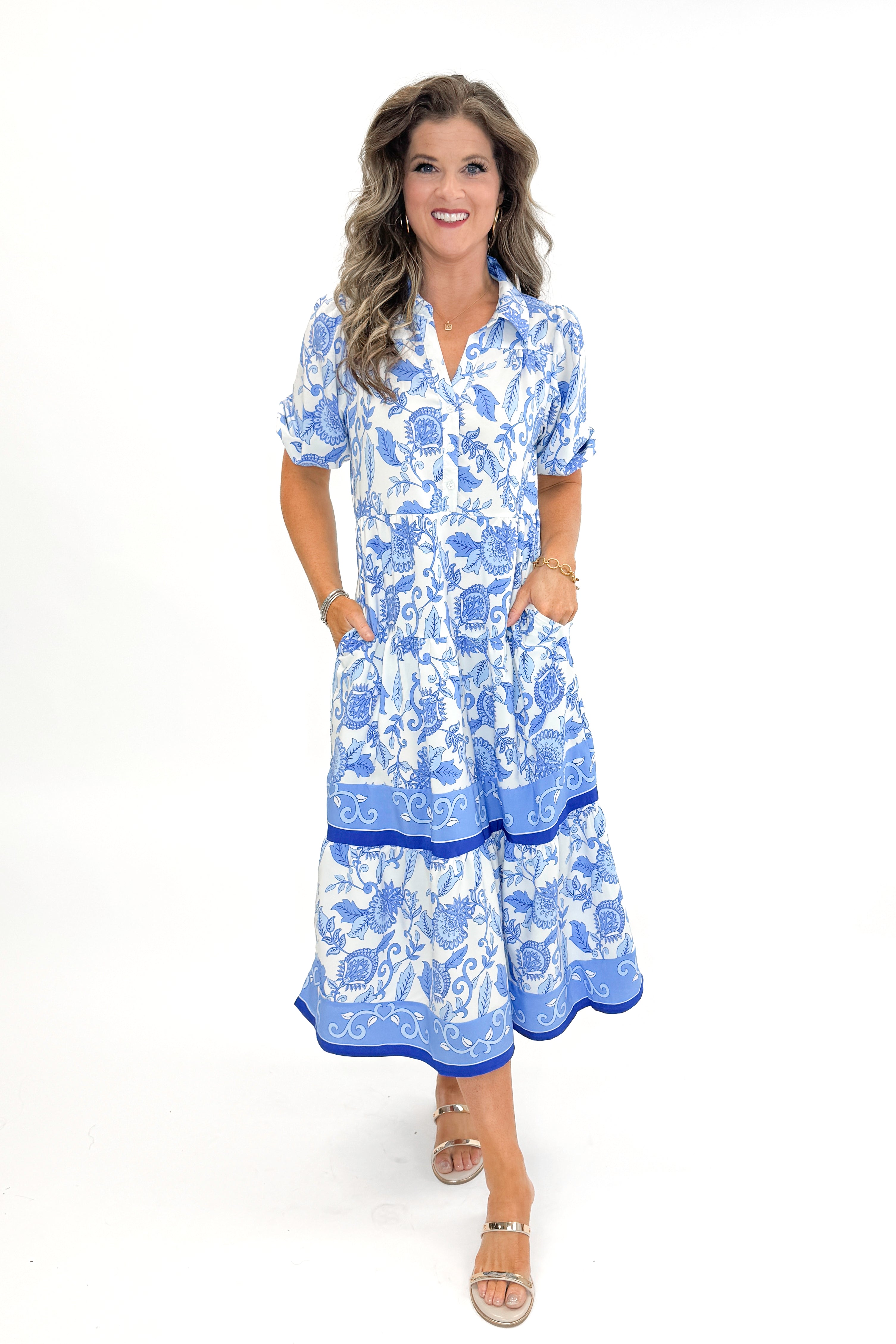 Front view of woman wearing Blue Floral Eloise Dress by Mary Square with sandals against white studio background.