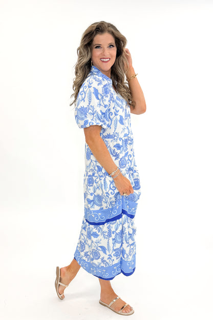 Side view of woman wearing Blue Floral Eloise Dress by Mary Square with sandals against white studio background.