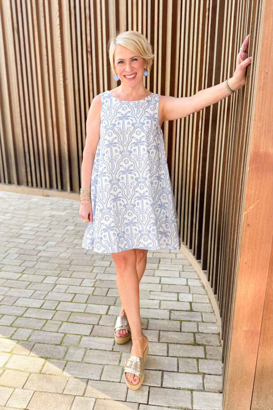 Woman wearing Pinch Blue Tropical Printed Mini Dress and sandals standing outside.